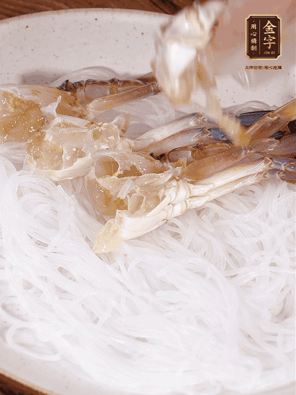 盤底墊上粉絲，擺上梭子蟹、火腿片，撒姜粒，淋上蒸魚豉油、花雕酒調(diào)味腌制15分鐘